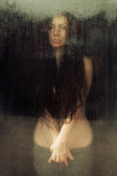 woman with long hair looking through wet glass