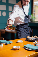 mano camarero sirve aceite de oliva en mesa de madera en interior de restaurante en cuenco blanco...