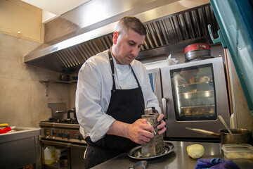chef  usa rallador metalico patatas en interior cocina de restaurante con uniforme blanco y mandil negro 