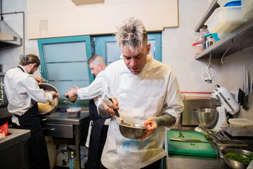 chef bate huevo en un bol metalico para steak tartar en cocina de restaurante con uniforme y...