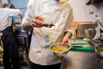mano chef vierte salsa de soja en un bol metalico prepara un steak tartar con uniforme blanco en interior de cocina restaurante close-up