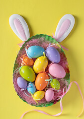 Easter colorful eggs in plate as egg and bunny ears gingerbread on yellow background, Vertical greeting card, Top view