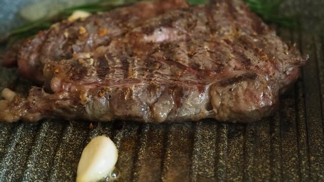 Juicy beef meat steak with garlic cooking on griddle pan at professional kitchen. Prime steak frying at grill. Delicious, modern cuisine