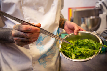 mano chef selecciona con pinzas brotes verdes en un bol metalico close-up