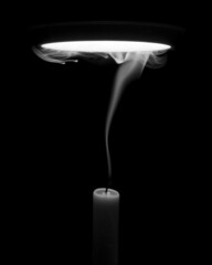 Grayscale of an extinguished candle with white smoke in the dark under the lamp