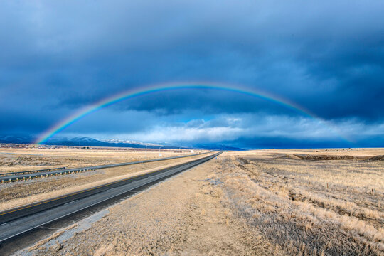 An interstate road reaching to the horizon through a flat landscape, rainbow above the road.