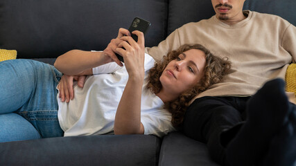 Woman spending time on her phone while boyfriend watching TV in sofa at home