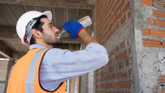 Middle Eastern handsome engineer drinking water to quench thirst. Drinking enough water on hot days.workers are tired from work.Image of a person holding a water bottle and drinking it all.