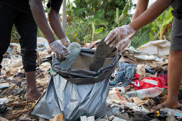 Close-up of the hands of two african guys collecting rubbish left on the street with a garbage bag,...
