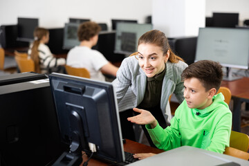 Obraz premium Smiling female teacher talking approvingly to happy preteen student sitting at computer in classroom, praising correctly completed assignment