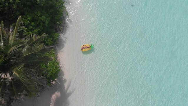 Aerial drone quad copter footage of nice woman girl floating on a lilo inflatable with in tropical waters in maldives of crystal clear waters of an ocean coral reef with palms