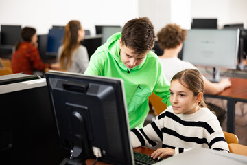 Fototapeta premium Smart interested preteen schoolboy helping cute girl classmate sitting at computer during informatics lesson..