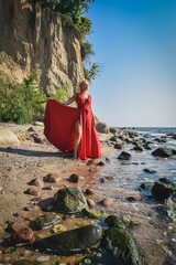 Creative holiday seaside session. Beautiful woman on the seashore in an elegant red dress.