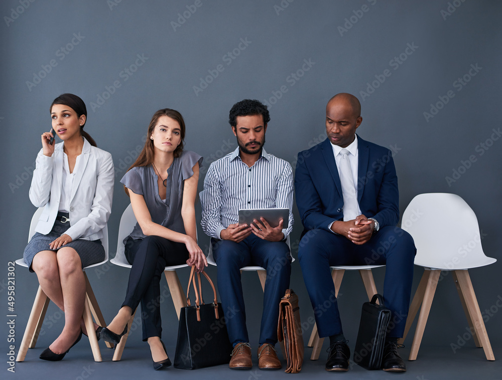 Poster trying to stay occupied while we wait. studio shot of a group of corporate businesspeople waiting in