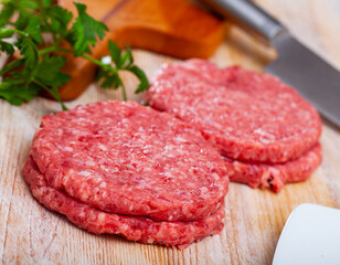 Raw meat cutlets with parsley on wooden cutting board