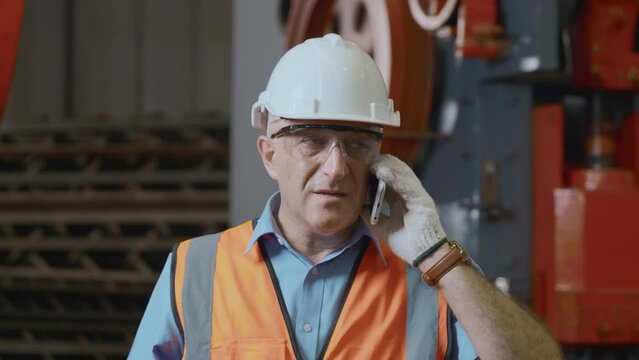 Cuasian worker man technician wear safety uniform with hardhat have problem during working he call mobile phone with smartphone to engineering and talking in metal sheet factory industry workshop