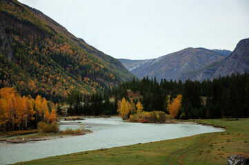 A bend of a turquoise beautiful river flowing through an autumn valley surrounded by mountains.