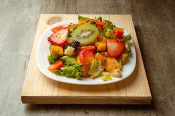 Bowl of healthy fresh fruit salad with fried chicken on a wooden base