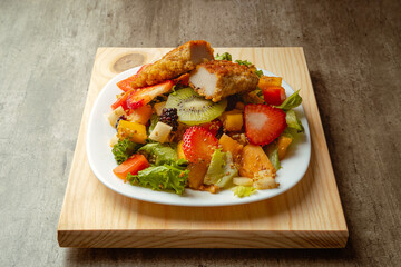 Bowl of healthy fresh fruit salad with fried chicken on a wooden base