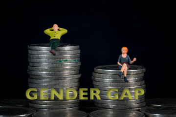 Miniature people sitting on a pile of coins. The concept of income distribution gender gap. Macro