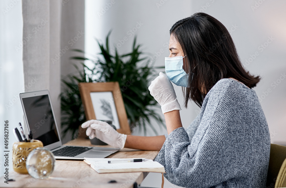 Poster powering through in the name of productivity. shot of a masked young woman coughing while working fr