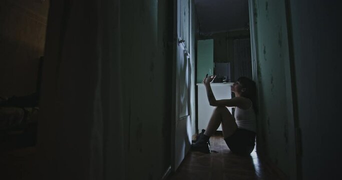 Woman smoking weed in corridor. Zoom in view of female junkie igniting and smoking marijuana joint while sitting on floor in dark hallway at home