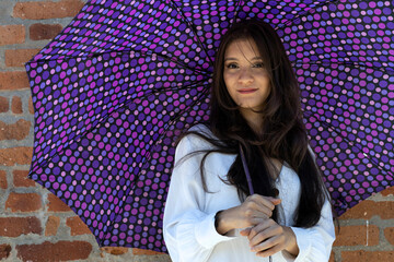 Portrait of beautiful young Latin American woman (24) posing while holding a purple umbrella with circles patterns. Lifestyle concept