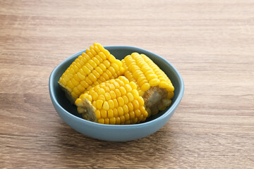 Jagung manis rebus or boiled sweet corn slices served on bowl on wooden background. Space for text. 

