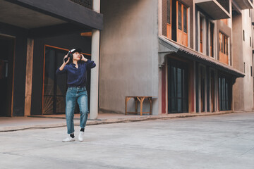 Happy young asian woman listening to music and having fun with headphones via smartphone on the street.