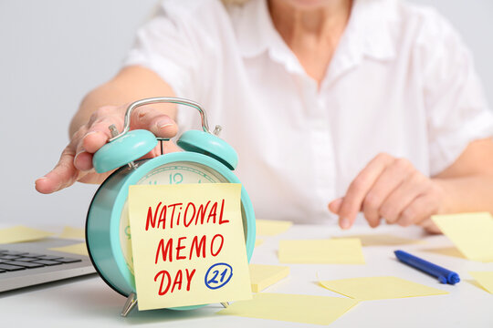 Alarm clock and sticky note paper with text NATIONAL MEMO DAY on table of mature secretary - Powered by Adobe