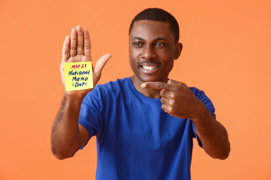 African-American man with note paper sheet on his palm against color background. National Memo Day - Powered by Adobe