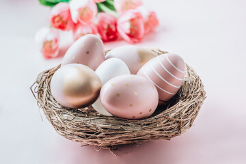 Beautiful pink tulips with pink and gold eggs in nest on light pink background.