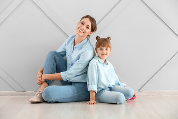 Portrait of happy mother and daughter sitting on floor near wall