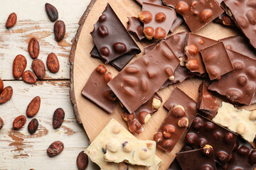 Board with pieces of tasty chocolate and nuts on table