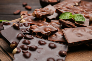 Pieces of tasty chocolate with hazelnuts on board, closeup