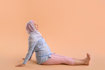 Pregnant Muslim woman doing yoga on beige background