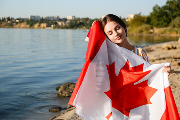 Beautiful young woman with flag of Canada near river