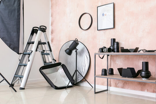 Shelving unit with lighting equipment and ladder near pink wall in photo studio