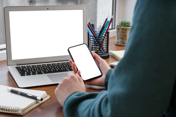 Woman with mobile phone sitting at table with modern laptop