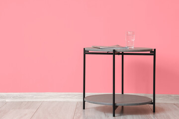 Table with glass of water and magazine near color wall