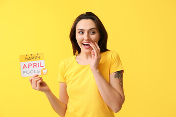 Happy young woman with card on yellow background. April fools' day