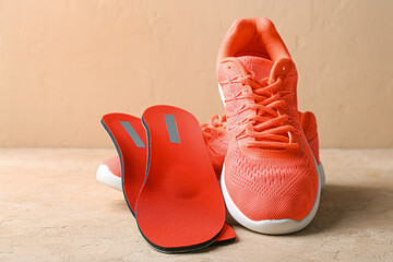 Orthopedic insoles and sneakers on beige background