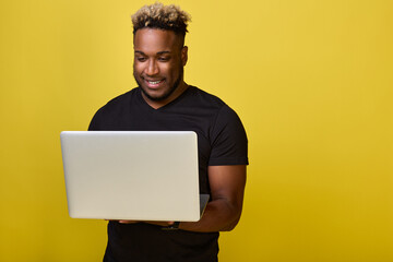 Handsome, muscular guy holds a laptop and reads an email. Smiling black guy communicates in social networks with friends by correspondence using a modern laptop