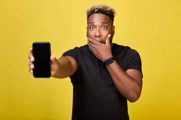 Surprised tall black man holds mobile phone in his hand covering his mouth with his hand. Cute...