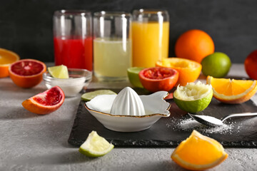 Ceramic juicer, sugar and citrus fruits on grey background
