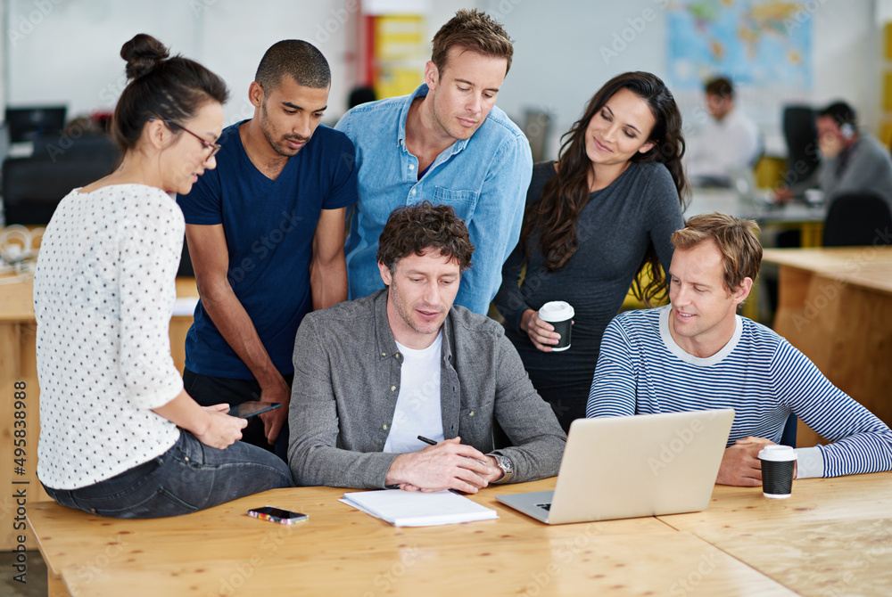Poster the merging of creative minds. shot of a group of colleagues using a laptop together in a casual wor