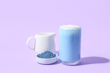 Obraz na płótnie Canvas Glass of blue matcha tea, jug with milk and bowl with powder on purple background