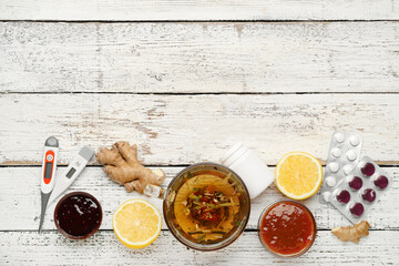 Cup of tea, pills for sore throat, lemons, ginger, jam and thermometer on white wooden background