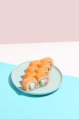 Classic sushi roll with salmon outside, crab, cheese and cucumber inside. Philadelphia maki in minimal style. Modern japanese menu concept. Salmon maki roll on ceramic plate on coloured background.
