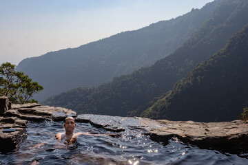 man enjoying the pristine view at natural swimming pool at mountain cliff from top angles